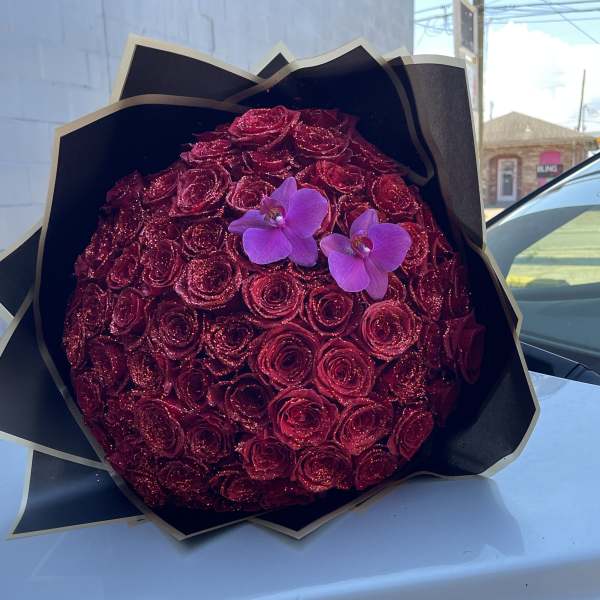 Round bouquet of red roses with two purple orchids in black wrap