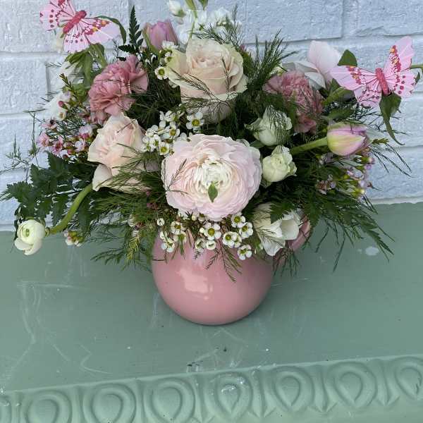 Pink and white floral arrangement in a pink vase with butterfly picks