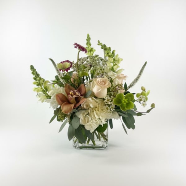 Mixed floral arrangement in a clear glass vase with cream, green, and purple blooms