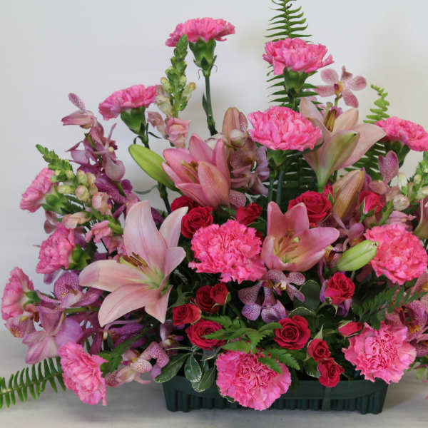 Fan-shaped arrangement of pink lilies, carnations, roses, and orchids in a green container