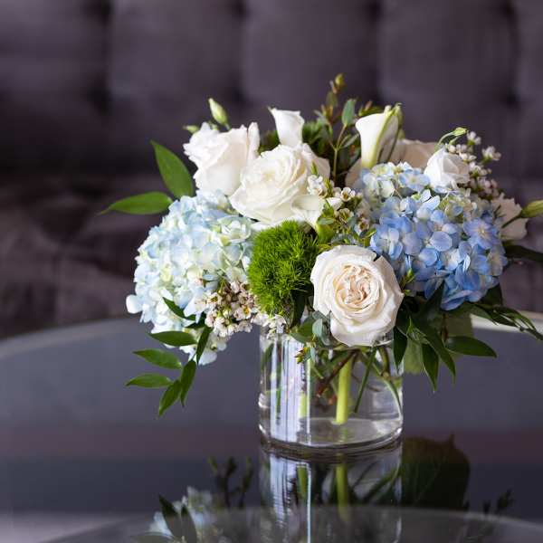 White roses and blue hydrangeas arranged in a clear glass vase