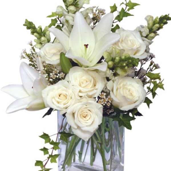 White lilies and roses arranged with accent blooms in a clear rectangular glass vase