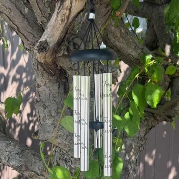 Silver wind chimes hanging from a tree branch among green leaves