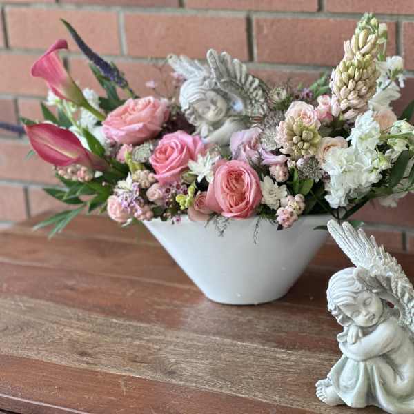 Pink and white floral arrangement in a white bowl with angel figurines