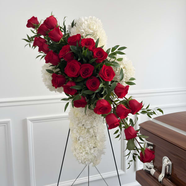 Red roses and white flowers arranged on a standing easel beside a casket