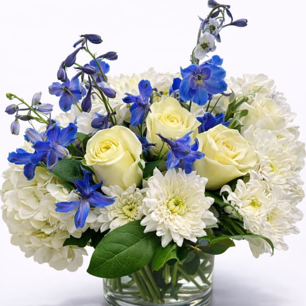 White and pale yellow roses with blue flowers in a glass vase