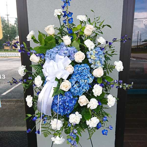 Standing floral spray with blue hydrangeas, white roses, and a white ribbon