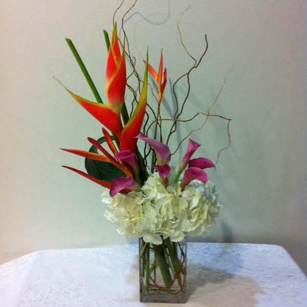 Tropical bouquet with red heliconia, purple calla lilies, and white hydrangea in a glass vase