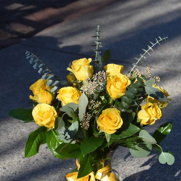 Arrangement of yellow roses with a yellow ribbon bow in a clear glass vase.