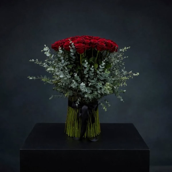 Red roses arranged in a black-wrapped bouquet with eucalyptus