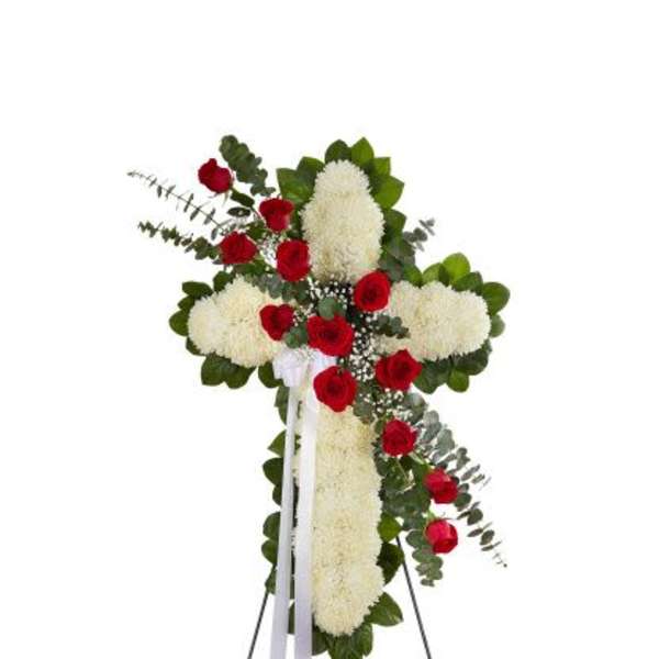 Standing cross of white flowers with red roses and white ribbon on a metal easel