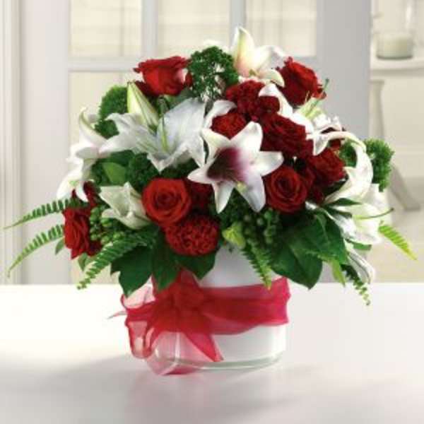 Red roses and white lilies arranged in a clear vase with a red ribbon
