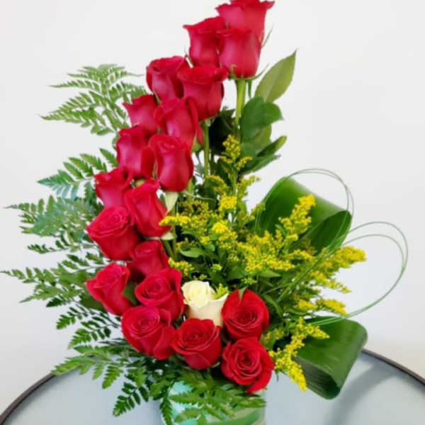 Red roses arranged in a clear glass vase with yellow filler flowers
