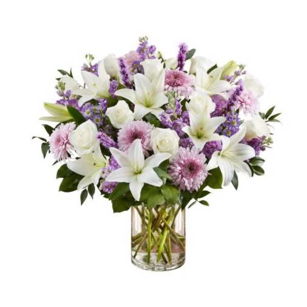 Arrangement of white lilies, white roses, and lavender flowers in a clear glass cylinder vase