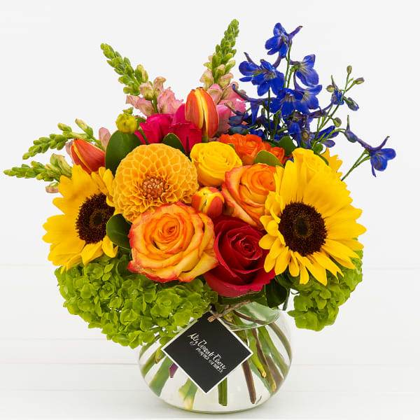 Bright mixed bouquet in a round glass vase with sunflowers and roses