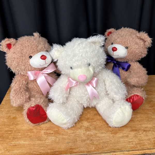 Three teddy bears with satin bows sitting on a wooden surface