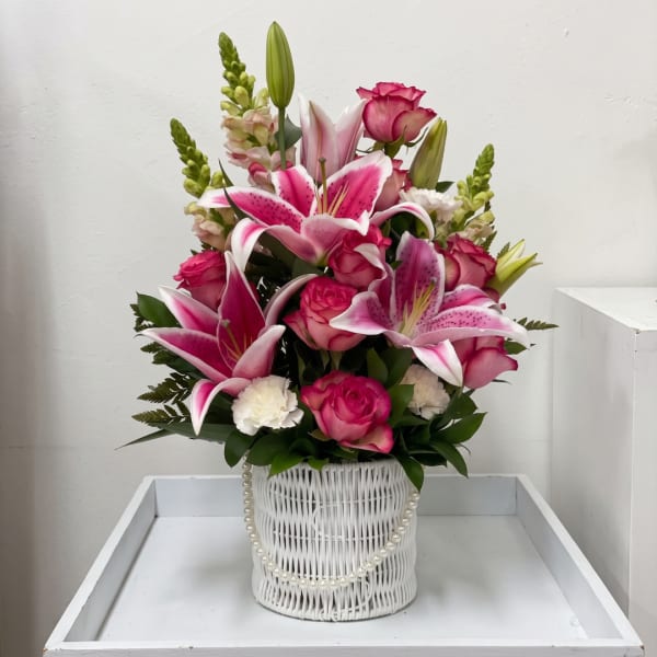 Pink lilies and roses arranged in a white basket with pearl trim
