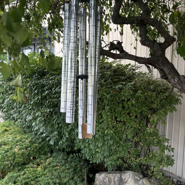Silver memorial wind chimes hanging from a tree in a garden