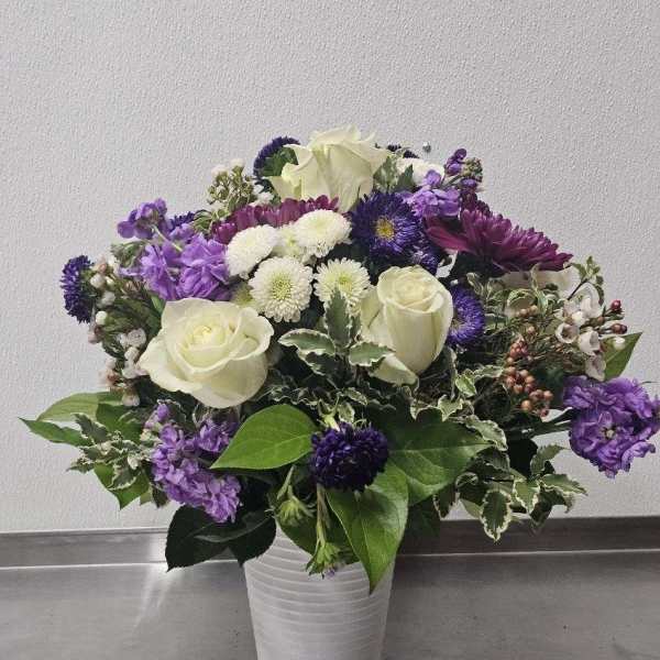 White roses and purple mixed flowers arranged in a white ceramic vase
