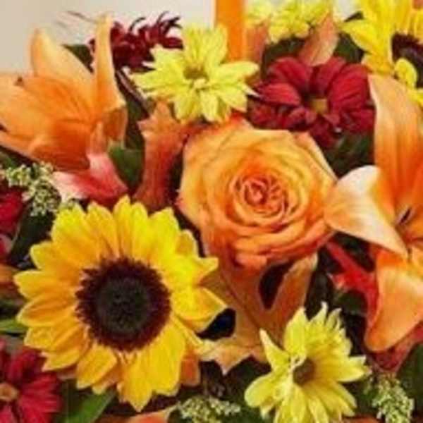 Colorful flower arrangement with sunflowers, roses, and lilies around a tall orange candle
