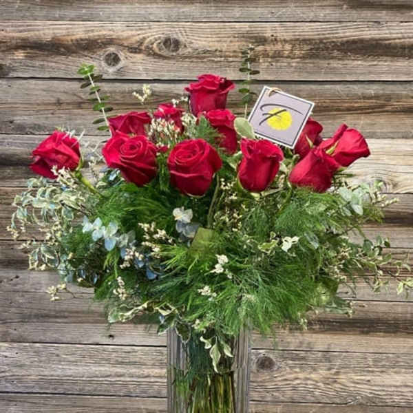 Red roses arranged in a tall glass vase with mixed greenery