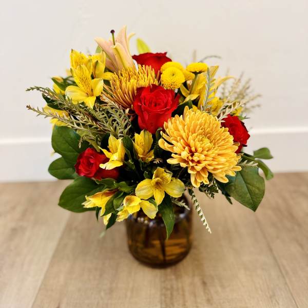 Bouquet of red roses and yellow flowers in an amber glass vase