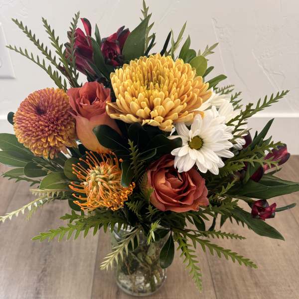 Mixed bouquet of orange, white, and burgundy flowers in a glass vase