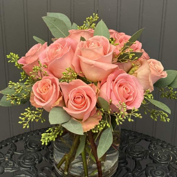 Pink roses arranged in a clear glass vase with greenery