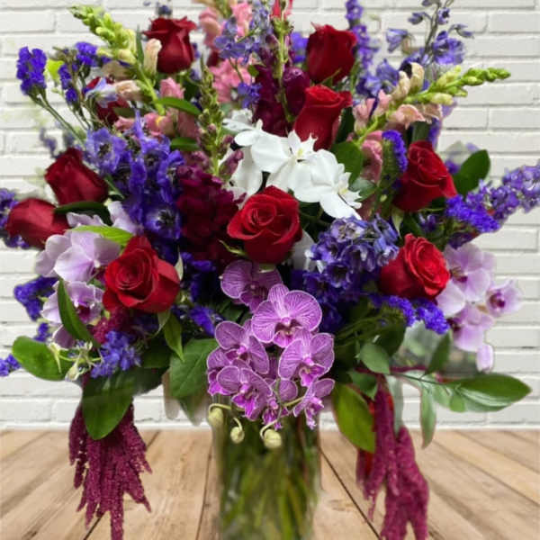 Bouquet of red roses, purple orchids, and white flowers in a glass vase