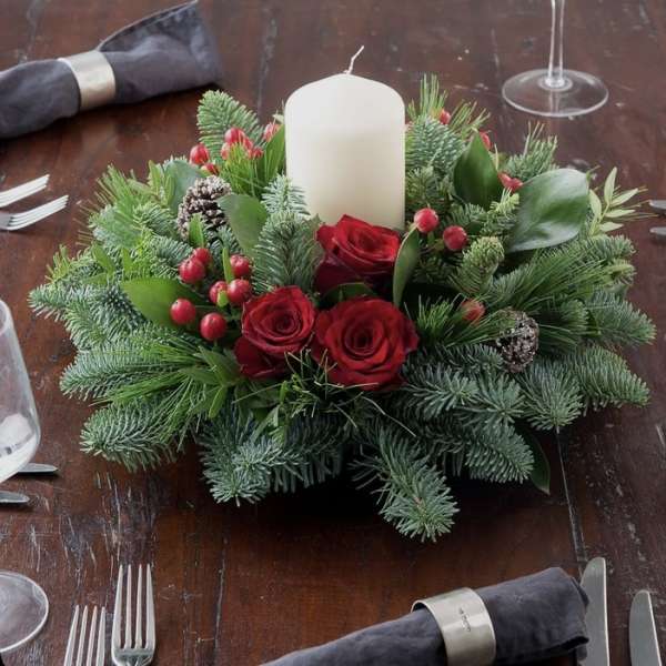 Red roses and greenery arranged around a white pillar candle on a table
