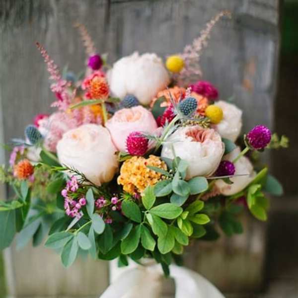 Hand-tied bouquet of pale roses and colorful accent flowers with a white ribbon