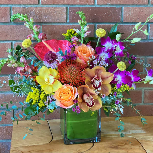 Colorful mixed tropical and garden flower arrangement in a rectangular glass vase