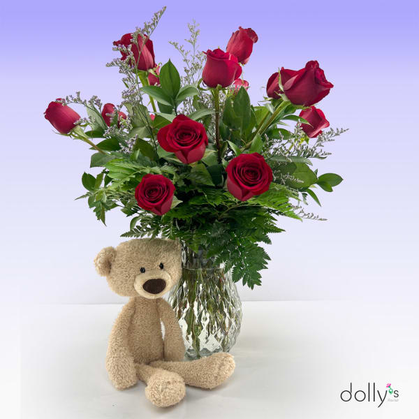 Red roses in a glass vase with a teddy bear in front