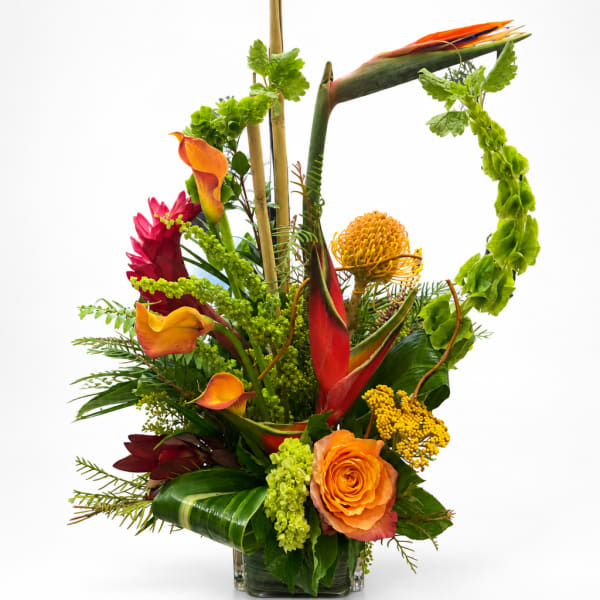 Tropical floral arrangement with orange roses, calla lilies, and bright green accents in a glass vase