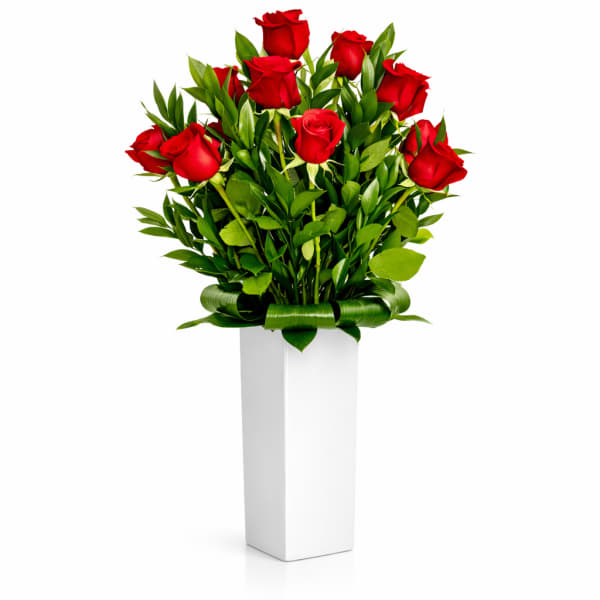 Red roses arranged in a tall white vase with green foliage