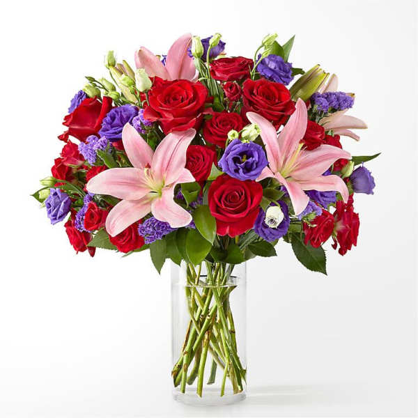 Bouquet of red roses, pink lilies, and purple blooms in a clear glass vase