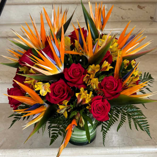 Bouquet of red roses and orange bird of paradise in a glass vase