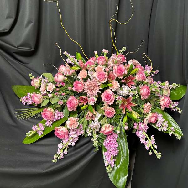 Pink roses and lilies arranged with trailing purple flowers on a black drape