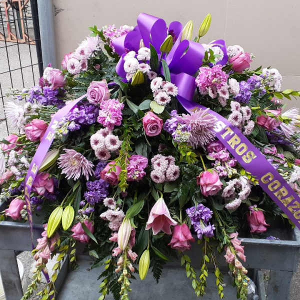 Large purple and pink funeral spray with ribbon on a stand