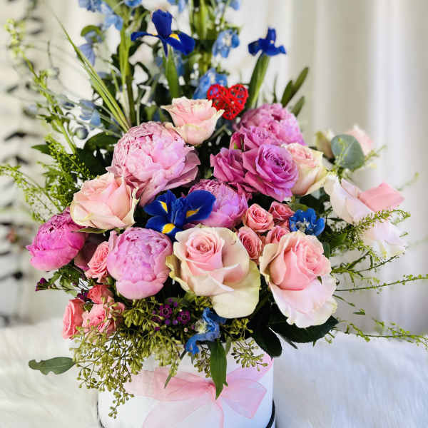 Pink roses and peonies arranged with blue irises in a white hat box