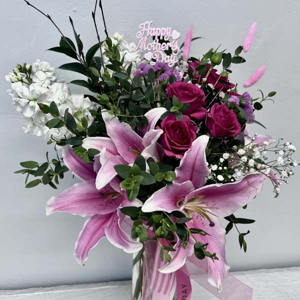 Pink lilies and roses in a glass vase with a Happy Mother's Day sign