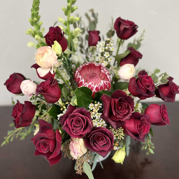 Bouquet of deep red roses with a pink protea and small white filler flowers