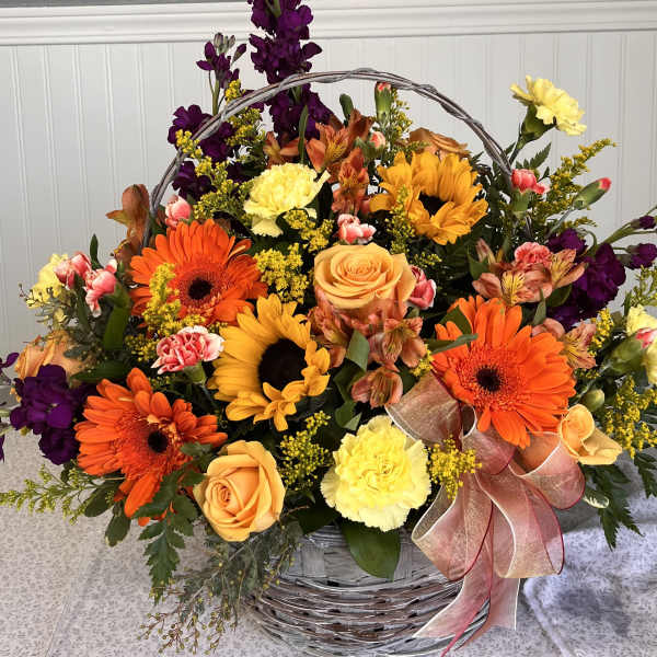 Basket arrangement of orange and yellow flowers with purple accents and a ribbon