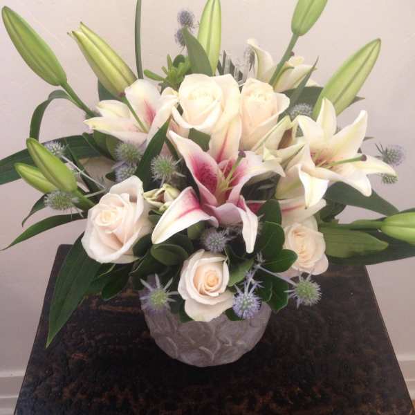 Compact arrangement of cream roses and pink lilies in a gray textured vase on a dark wooden table