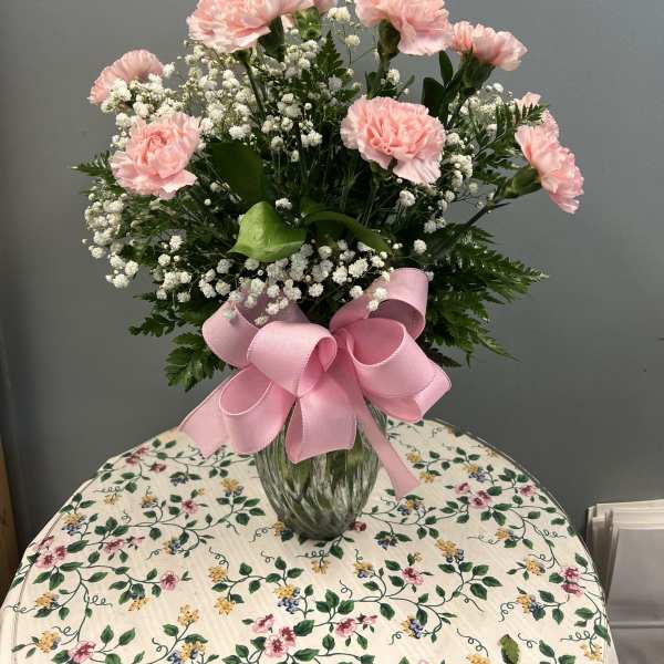 Pink carnations and baby's breath in a glass vase with a pink bow