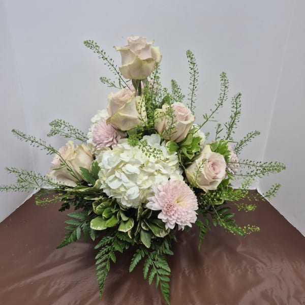 Arrangement of pale roses, white hydrangea, and pink mums in a low design