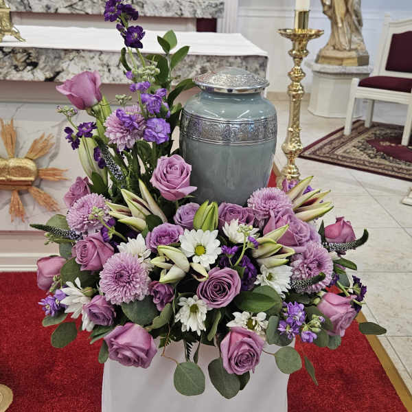 Lavender and white floral arrangement around a gray urn in a church