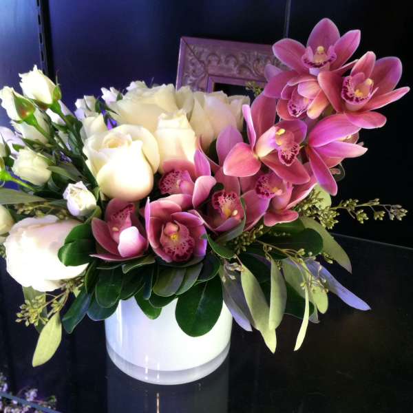 Low arrangement of white roses and pink orchids in a white cylinder vase