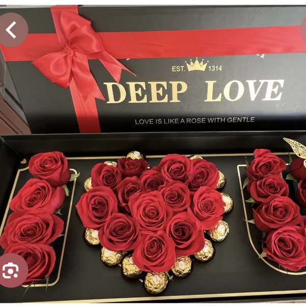 Red roses arranged in a gift box with chocolates and a ribbon bow