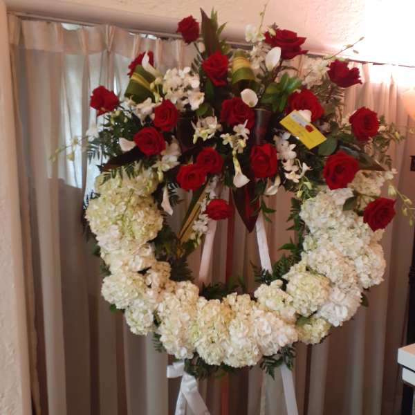 Standing floral wreath with red roses and white flowers on a ribboned easel